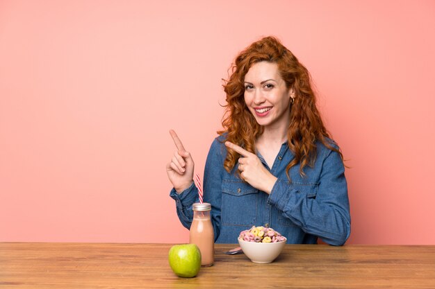 Mulher ruiva tomando cereais e frutas, apontando o dedo para o lado