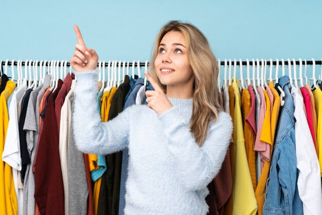 Foto mulher russa adolescente comprando roupas isoladas na parede azul apontando com o dedo indicador uma ótima idéia