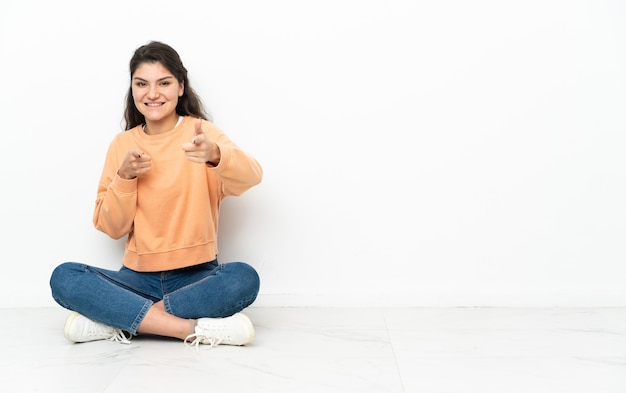 Mulher russa adolescente sentada no chão, apontando para a frente e sorrindo