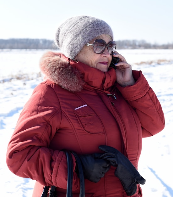 Mulher russa sênior falando ao telefone contra um campo nevado