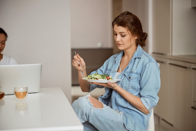 Mulher satisfeita cruzando as pernas enquanto saboreia sua refeição, estando na cozinha