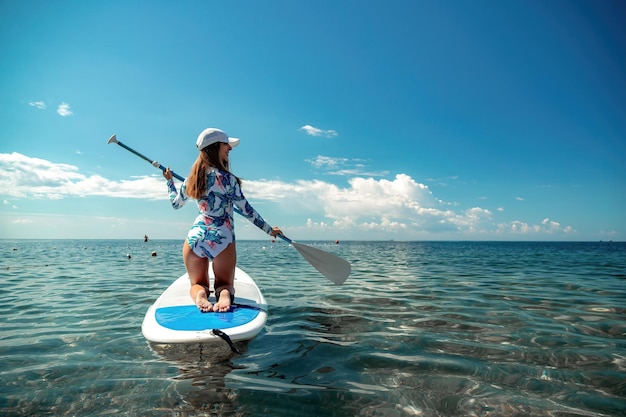 Mulher saudável e feliz em biquíni relaxando em uma prancha de surfe flutuando no mar azul-turquesa