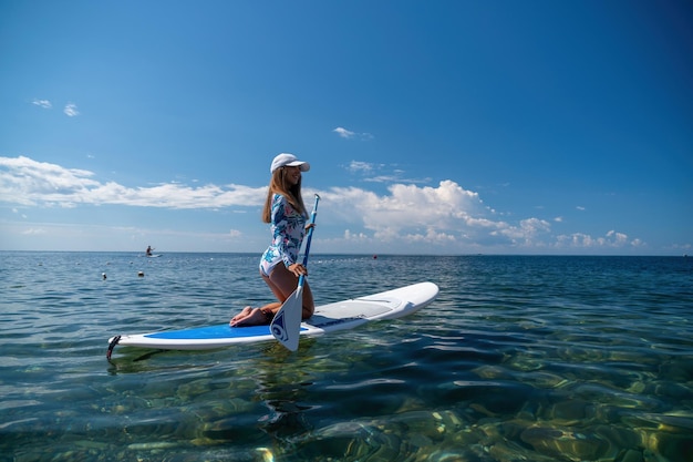 Mulher saudável e feliz em biquíni relaxando em uma prancha de surfe flutuando no mar azul-turquesa