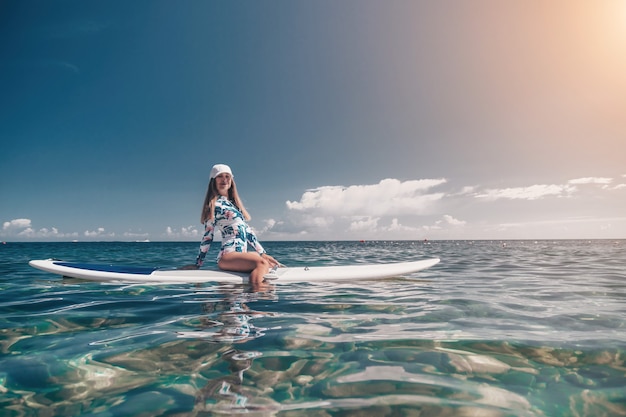 Mulher saudável e feliz em biquíni relaxando em uma prancha de surfe flutuando no mar azul-turquesa