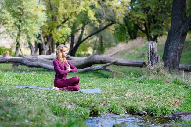 Mulher saudável faz meditação de ioga com namaste na floresta verde com tronco de árvore e atividade de fitness ao ar livre