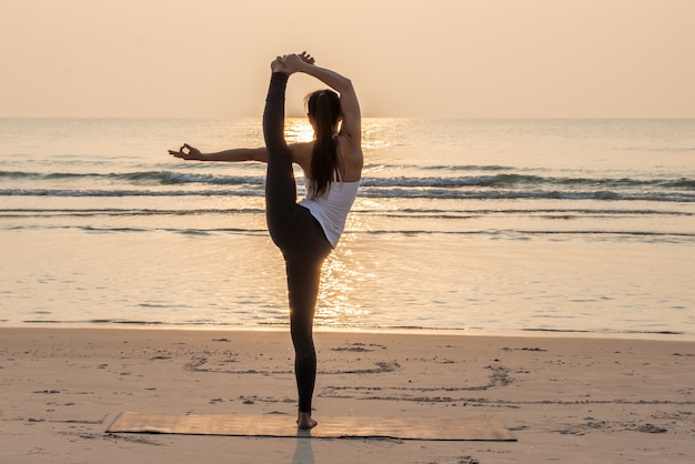 Mulher saudável que faz o pose da ioga na praia na manhã.