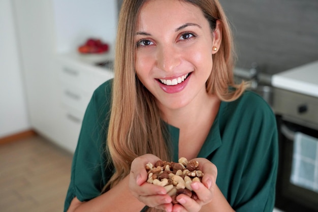 Foto mulher saudável sorridente mostrando uma mistura de nozes e frutas secas em suas mãos na câmera