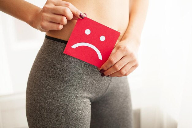 Mulher saúde corpo feminino segurando cartão triste smiley perto do estômago