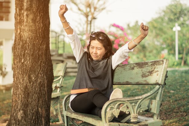 Foto mulher se alongando enquanto está sentada em um banco no parque