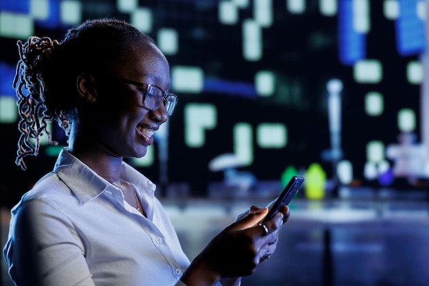 Mulher se divertindo andando pela cidade à noite, navegando na plataforma de compras on-line usando o celular. Cidadão afro-americano usando smartphone enquanto caminha pelas ruas vazias iluminadas por lâmpadas
