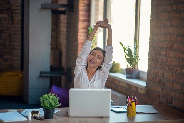 Foto mulher se espreguiçando enquanto está sentada à mesa no escritório