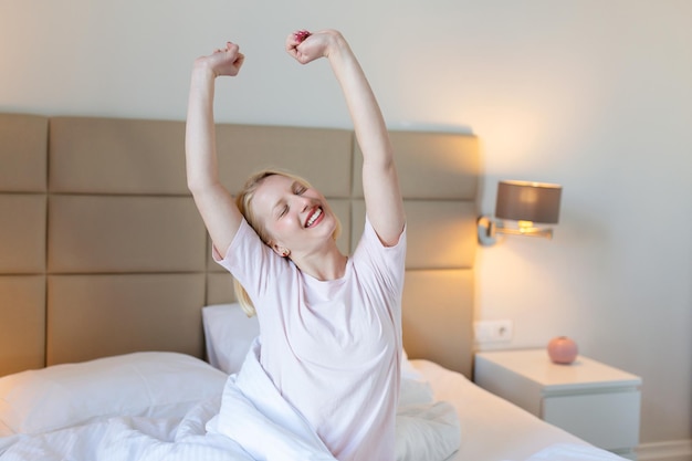 Mulher se esticando na cama com os braços levantados retrato de uma linda garota atraente aproveitando o tempo ruim depois de dormir deitada debaixo do cobertor fazendo alongamento mantendo os olhos fechados bom dia vida saúde