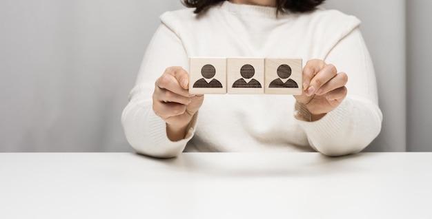 Mulher se senta à mesa e segura cubos de madeira. O conceito de recrutar uma equipe no mundo dos negócios, encontrando funcionários talentosos. Líder em um grupo de pessoas