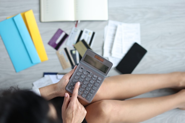 Mulher se senta no chão com a calculadora ao lado de cartões bancários e contas. conceito de planejamento e distribuição de orçamento