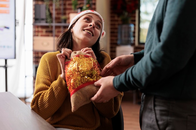 Mulher se sentindo feliz depois de receber o presente de natal no escritório de negócios, trocando presentes para celebrar a tradição do feriado de inverno. Pessoas alegres no local de trabalho decoradas com enfeites festivos.