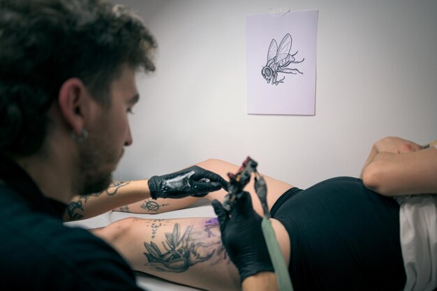 Mulher se tatuando na perna em um estúdio aconchegante decorado com obras de arte