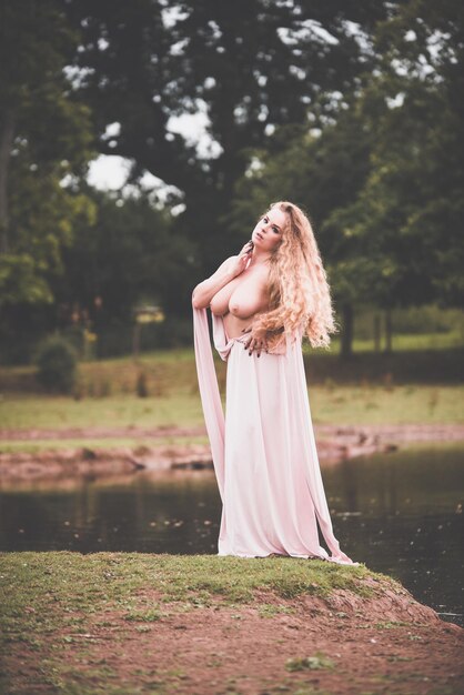 Foto mulher sedutora vestindo vestido de pé à beira do lago na floresta