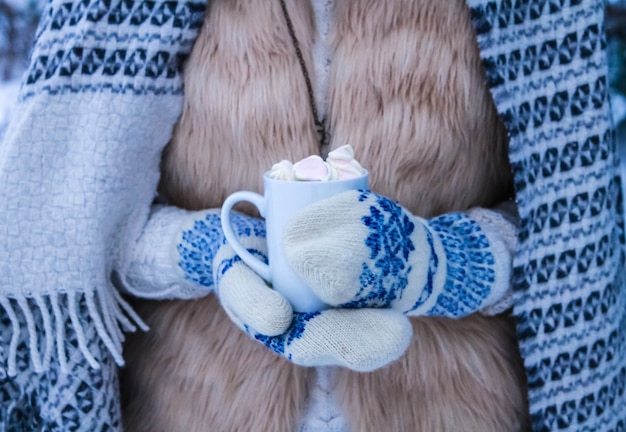 Mulher segura café com marshmallow na floresta de inverno