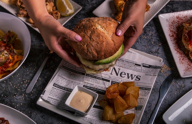 Mulher segura hambúrguer delicioso com as mãos e batatas fritas