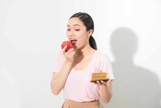 Mulher segura na mão bolo doce e maçã escolhendo, tentando resistir à tentação, fazer a escolha dietética certa. Conceito de gula do dilema da dieta de perda de peso.
