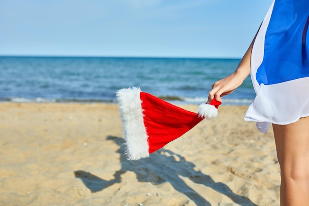 Mulher segura na mão chapéu de Papai Noel em pé na praia