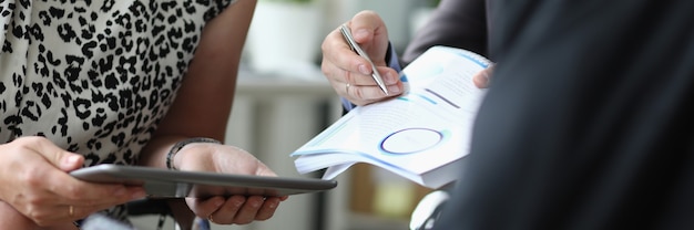 Foto mulher segura o tablet nas mãos ao lado dos homens com uma caneta esferográfica e documentos nas mãos no escritório closeup. conceito de assinatura de contratos de negócios.