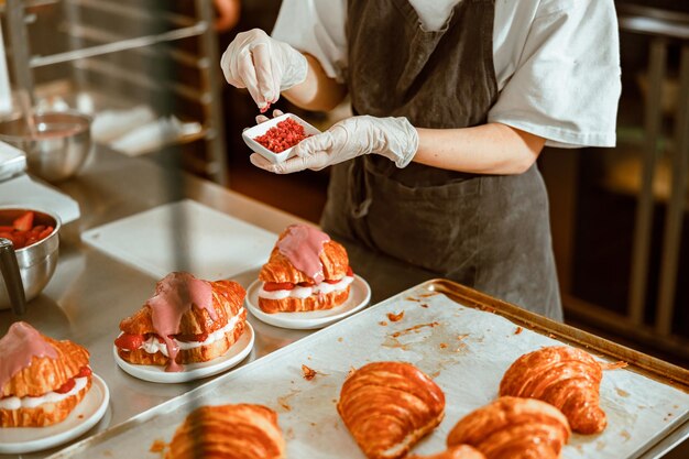 Mulher segura tigela pequena com borrifos rosa acima de croissants decorados frescos na mesa de metal