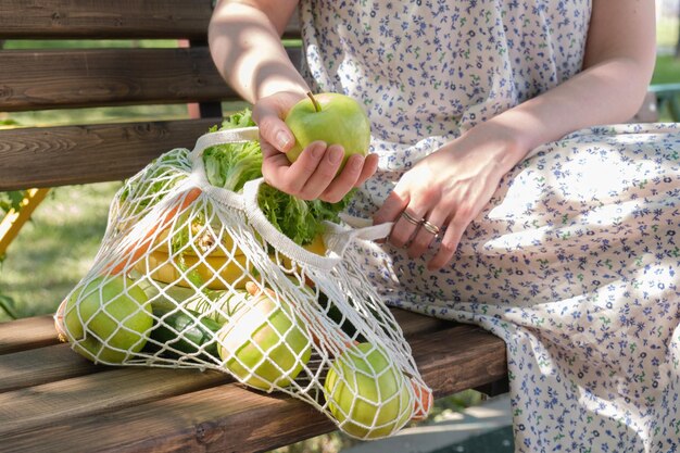 Mulher segura uma maçã verde na mão Saco de malha de malha com legumes e frutas