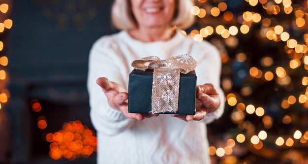 Mulher segurando a caixa de presente dentro de casa contra a árvore de Natal.