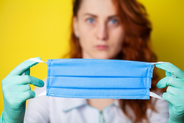 Mulher segurando a máscara para cobrir a boca e o nariz para proteger contra vírus em fundo amarelo.