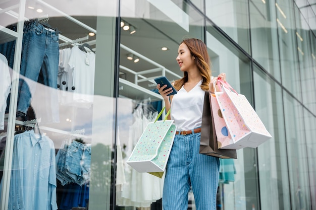 Mulher segurando a sacola de compras e o smartphone nas mãos perto da vitrine do shopping