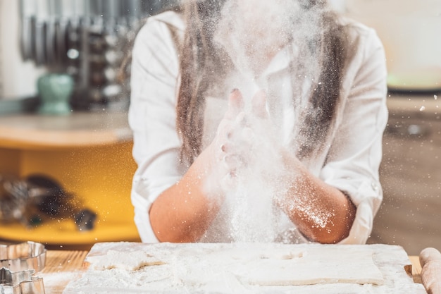 Foto mulher segurando as mãos cheias de farinha. explosão de pó branco