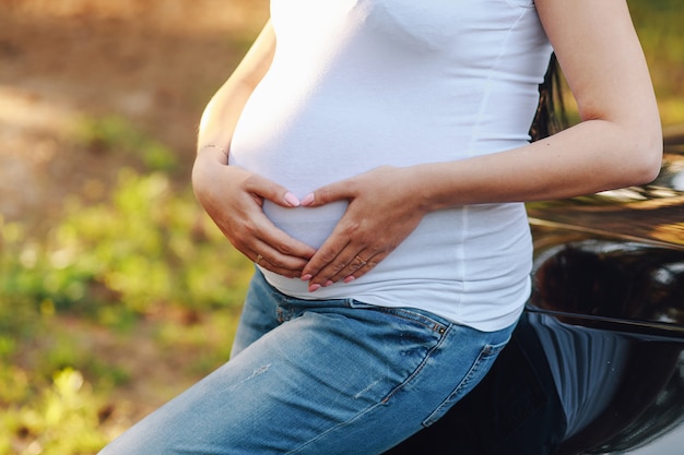 Mulher segurando as mãos em forma de coração na barriga dela grávida.