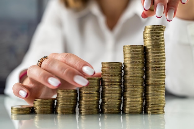 Mulher segurando as mãos perto de uma montanha de moedas em uma mesa ou na frente de pilhas de moedas