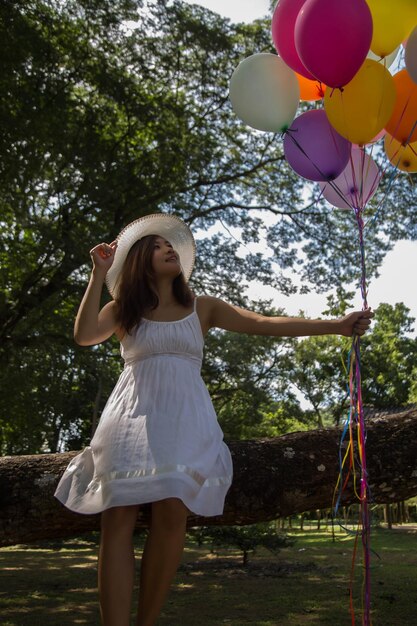 Foto mulher segurando balões enquanto está sentada no tronco da árvore