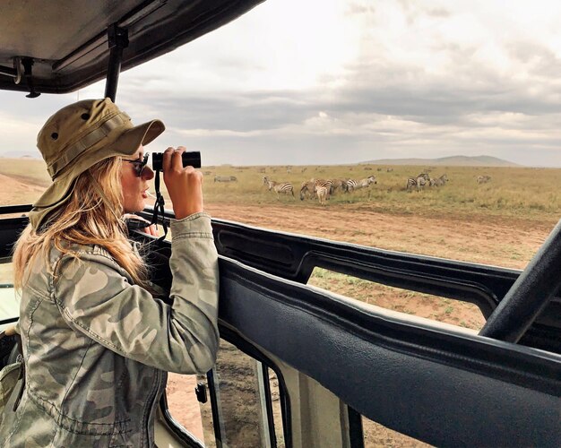 Foto mulher segurando binóculos enquanto está de pé em jipe contra o céu