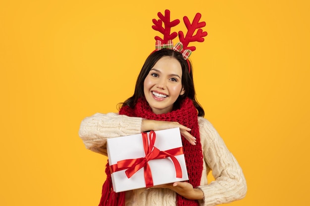 Mulher segurando caixa de presentes de Natal posando no estúdio de chifres festivos