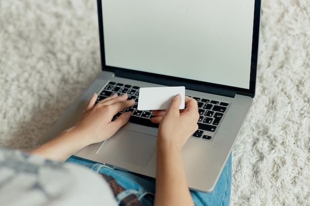 Mulher segurando cartão de crédito e trabalhando em um laptop mulher usando um laptop sentado no chão