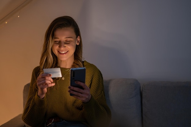 Mulher segurando cartão de crédito e usando smartphone enquanto faz compras online em casa