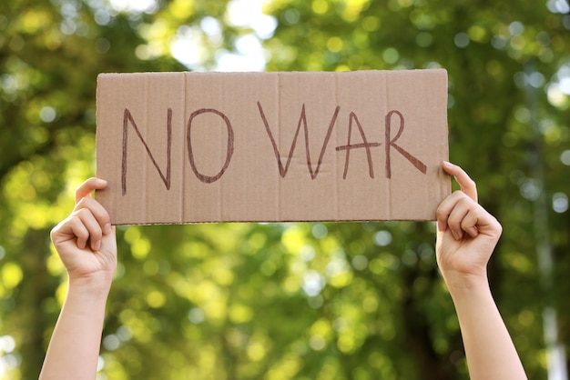 Foto mulher segurando cartaz com palavras sem guerra no parque closeup