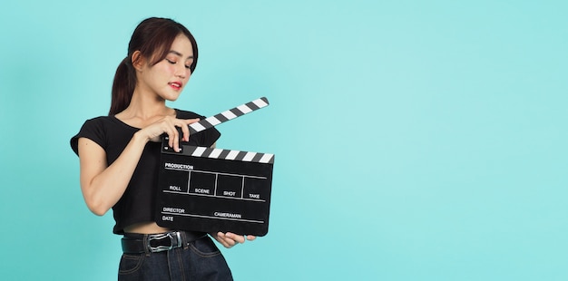 Mulher segurando claquete preta ou filme ardósia usar na produção de vídeo, cinema, indústria do cinema em fundo verde menta ou azul Tiffany.