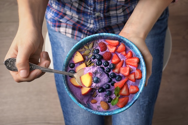 Mulher segurando colher e tigela com delicioso smoothie de açaí no café da manhã saudável, close-up