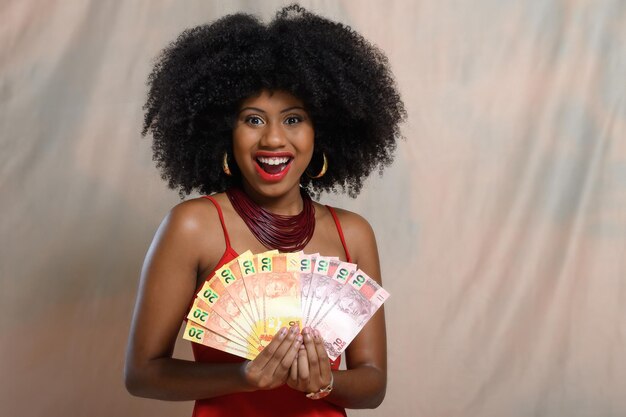 Mulher segurando dinheiro sorrindo menina negra segurando notas brasileiras positivamente surpreso gesturin