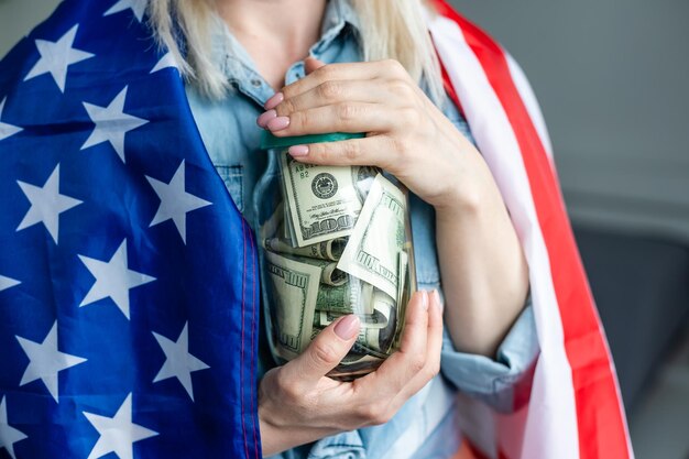 mulher segurando dólares em frasco de vidro e bandeira americana.