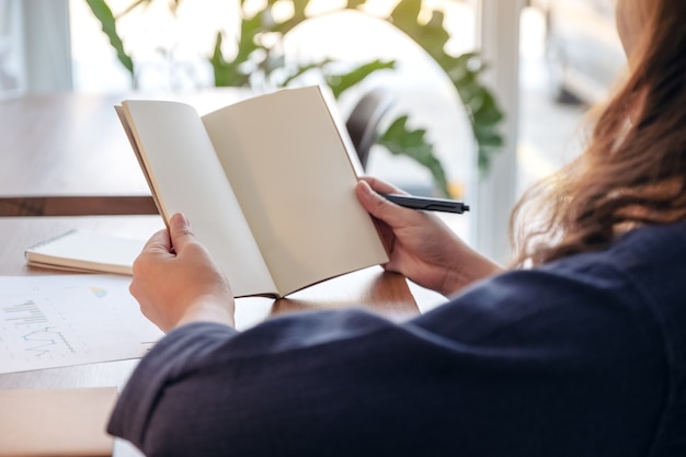 Mulher segurando e abrindo um caderno em branco na mesa de madeira