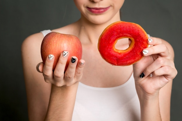 Mulher, segurando, e, fazer, escolha, entre, maçã vermelha, e, calorie, bomba, donut
