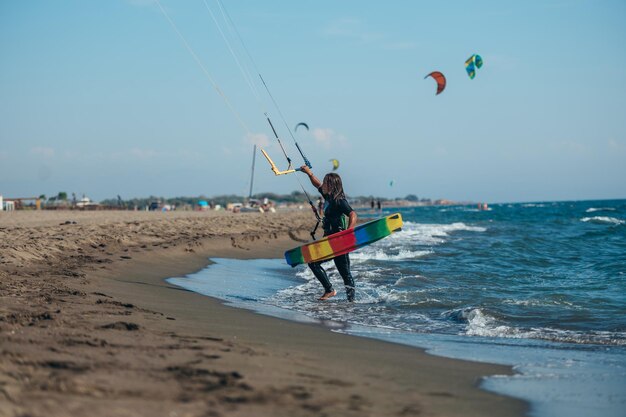 Mulher segurando kiteboard e entrando na água