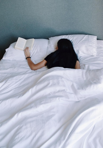 Mulher segurando livro enquanto dorme na cama em casa