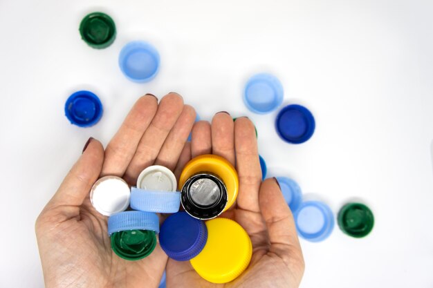 Mulher segurando muitas tampas de plástico coloridas de garrafas no fundo branco Conceito de reciclagem