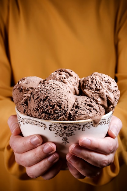 Mulher segurando nas mãos uma tigela vintage com muitas bolas de sorvete de chocolate. Deliciosa sobremesa de sorvete caseiro que está derretendo.